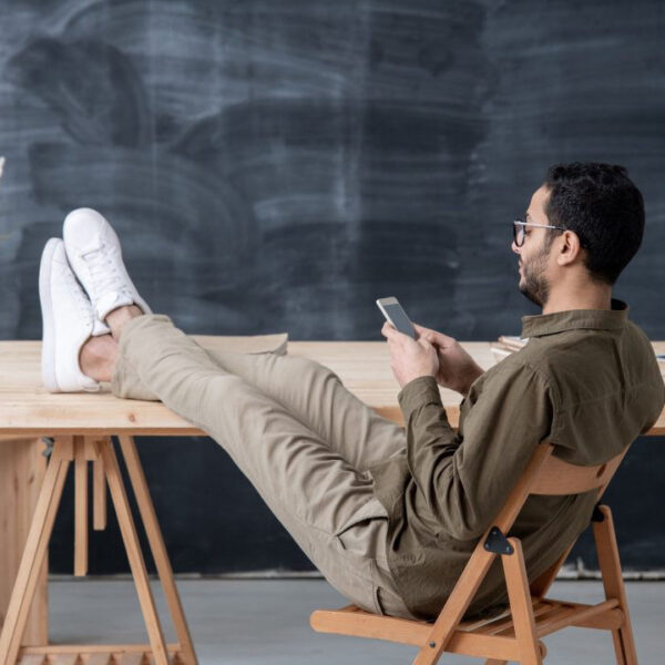 young-employee-in-casualwear-keeping-legs-on-table-while-scrolling-in-smartphone-1080x720