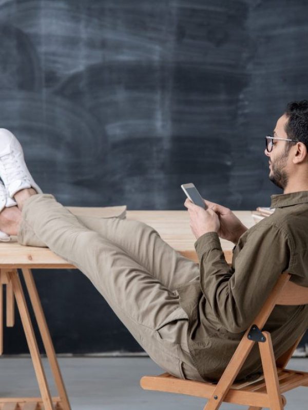 young-employee-in-casualwear-keeping-legs-on-table-while-scrolling-in-smartphone-1080x720